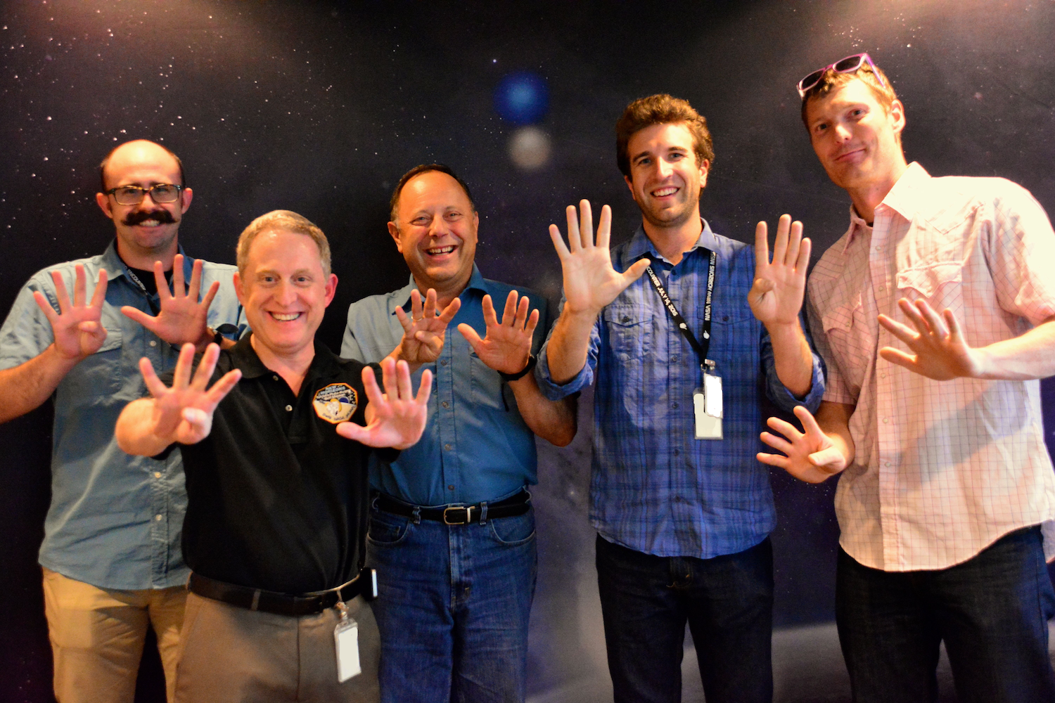 Five people pose for photo, each holding up 9 fingers