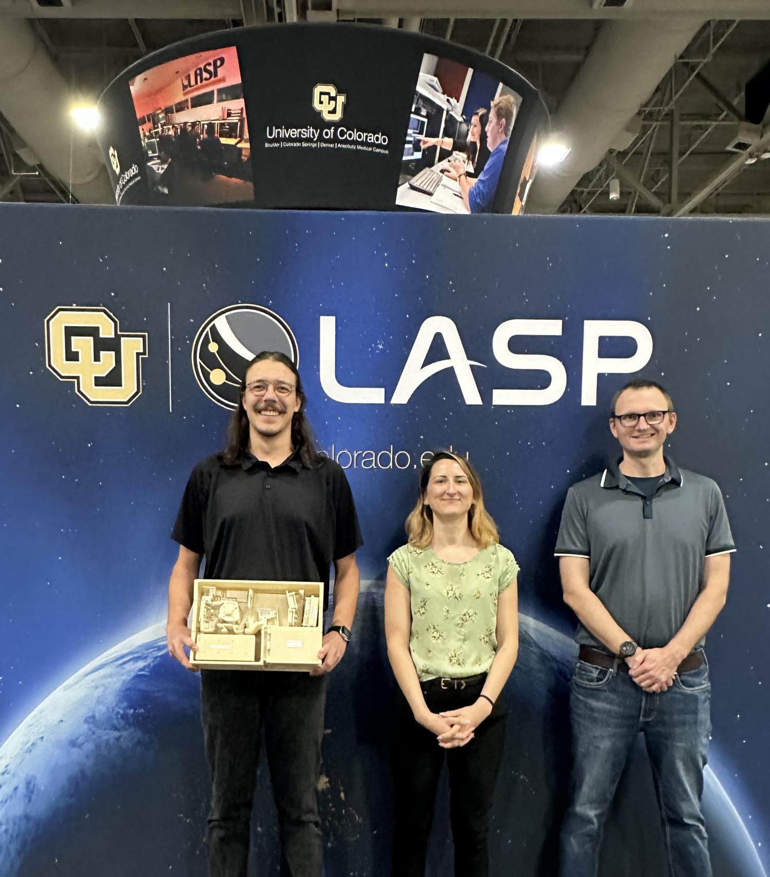 Three people pose in front of a banner reading "LASP."