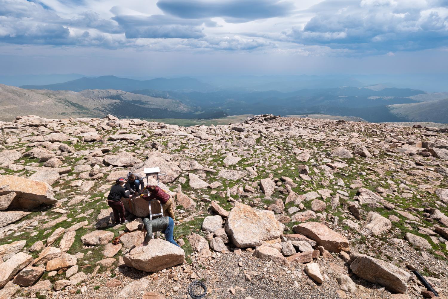 View from the summit of a mountain, with people seen in distance working on equipment