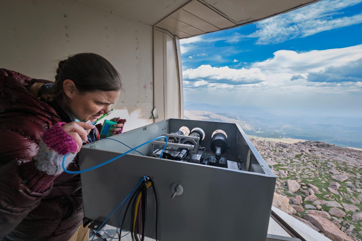 Woman works on scientific equipment with mountain view in background