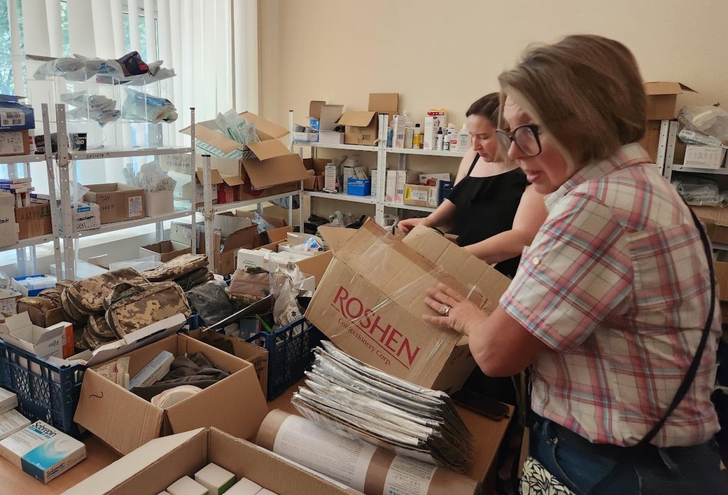 Two women unpacking boxes in a room filled with supplies