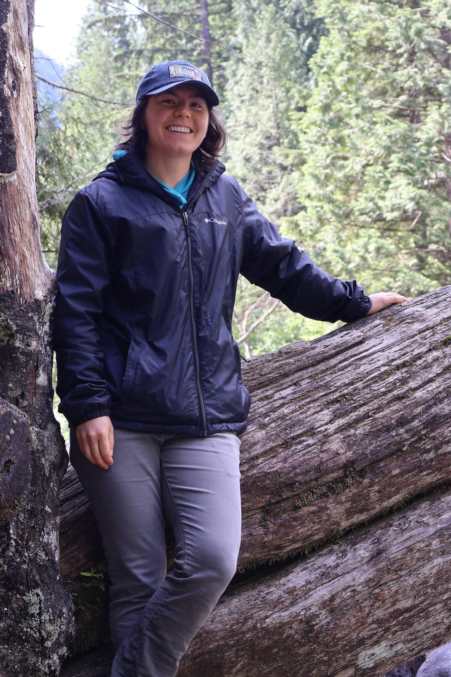 Woman stands in front of a log in the forest