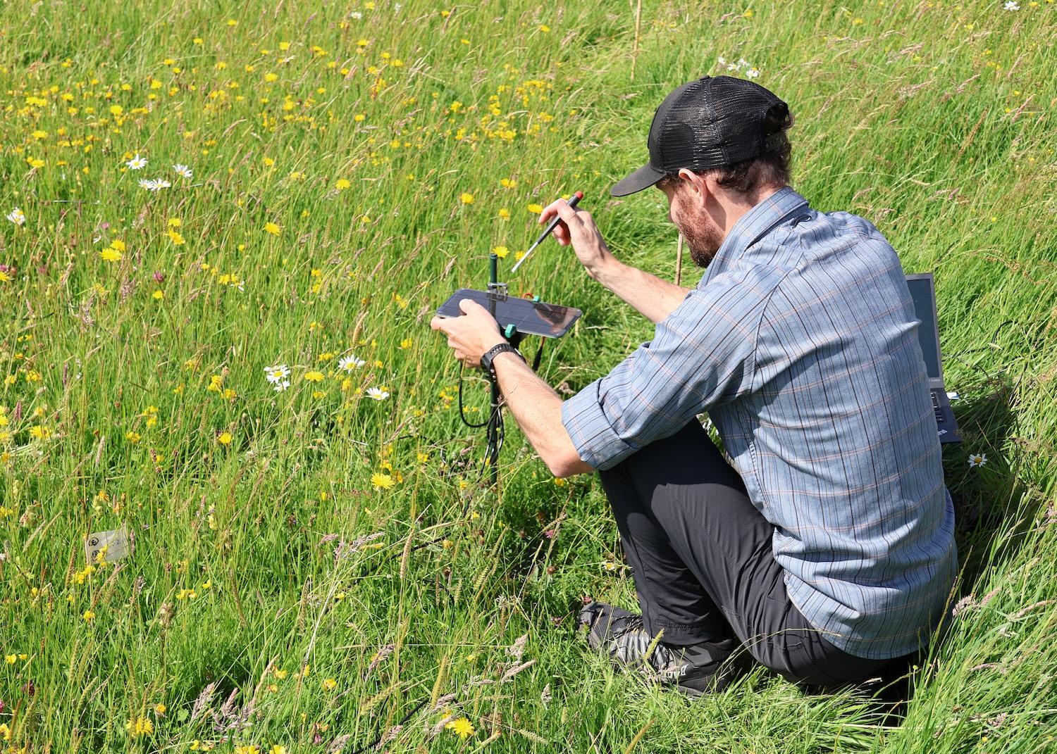 Man squats in field while working on electronics