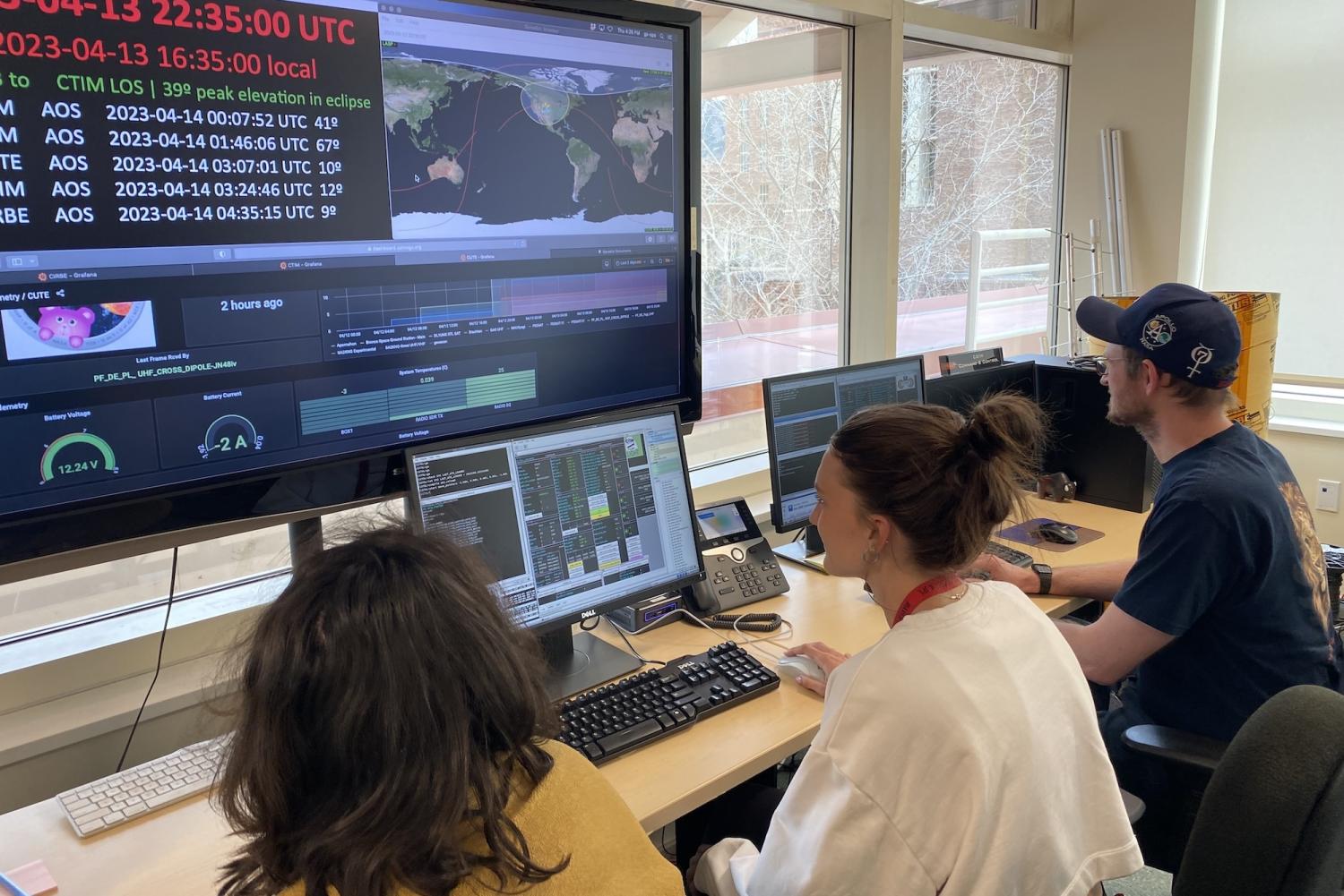 Three people seen from behind look at a large computer monitor