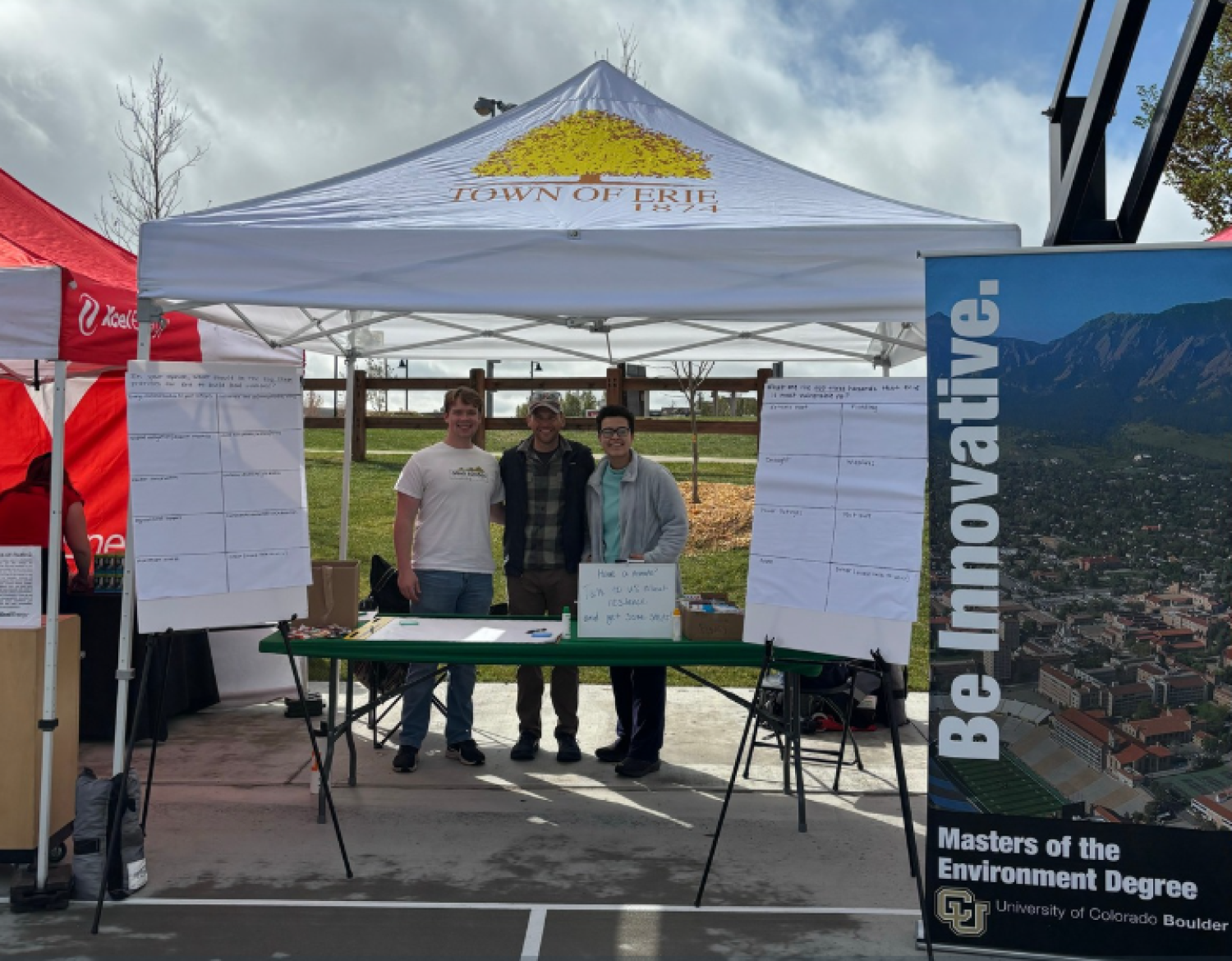 Students stand under a tent with a poster that says Be Innovative in front of them.