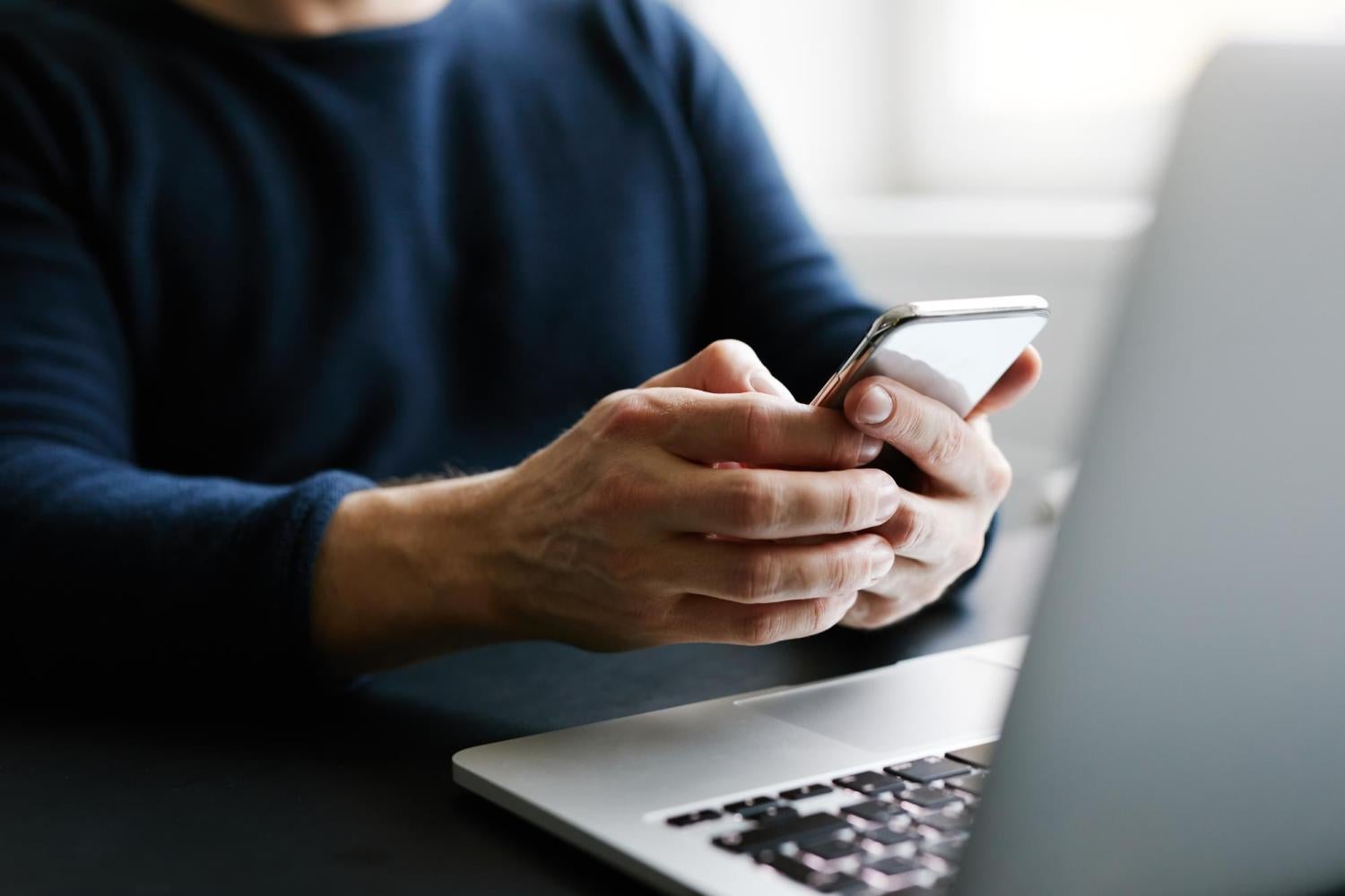 person checking phone and sitting near laptop