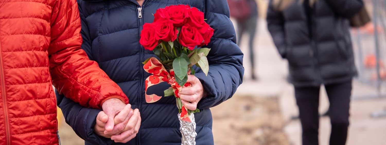 Two people holding hand and carrying red flowers