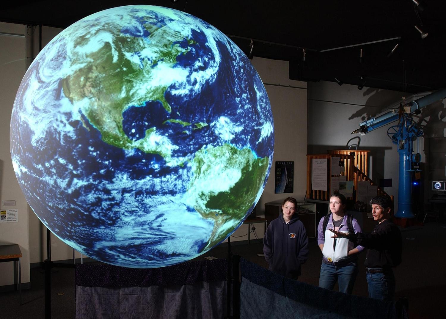 People look at an image of Earth projected on a sphere.