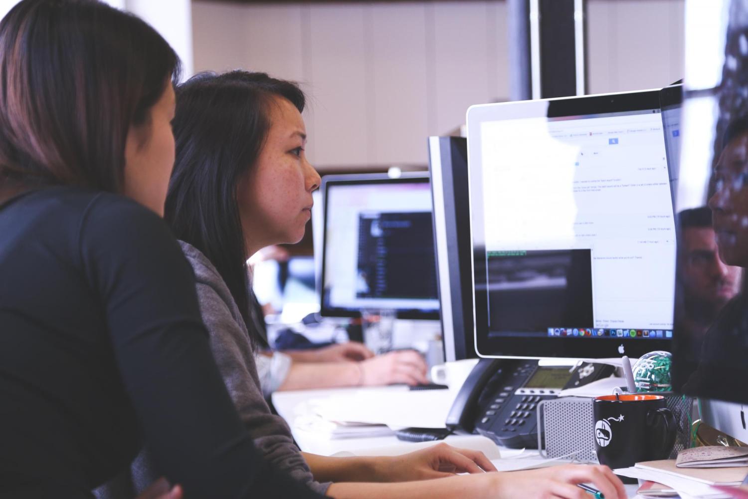 Two women work at desktop computers