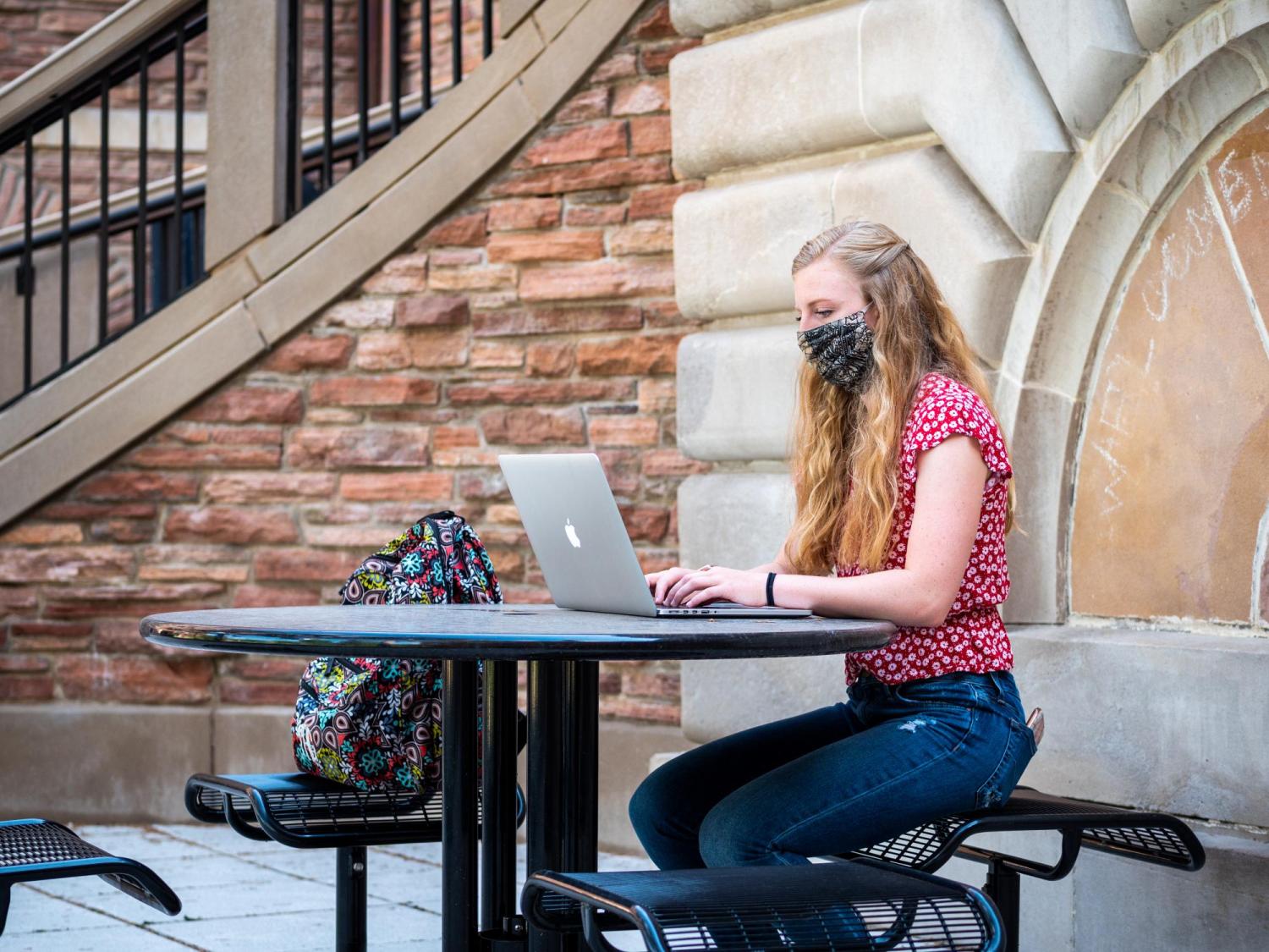 student working on computer on campus while wearing a mask