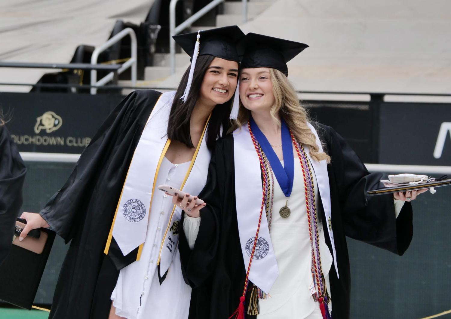 Two 2021 grads pose for a photo on Folsom Field during Grad Appreciation Days