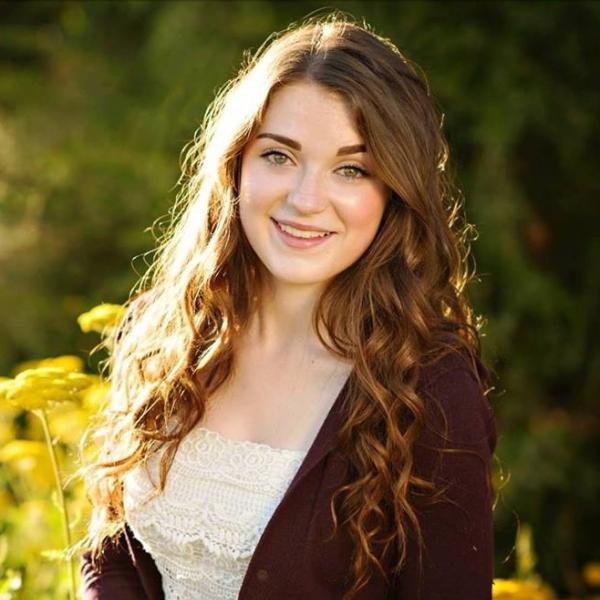 Lindsey stands outside with golden flowers behind her.