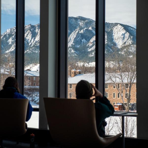 Students studying indoors, with snowy Flatirons in the distance.