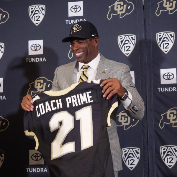 Sanders smiles and holds up a special jersey with his nickname during the press conference announcing his hiring.