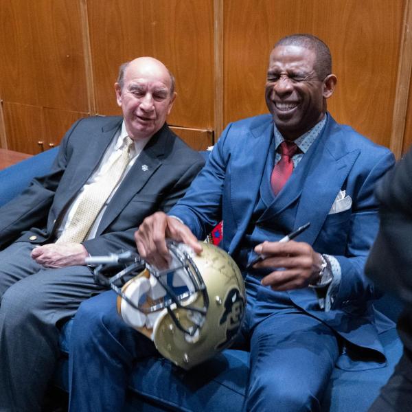 CU head football coach Deion Sanders laughs while adding his signature to a CU football helmet with signatures from previous CU coaches 