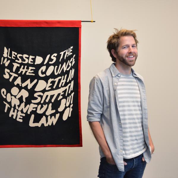 Matt Smith stands in front of his black and red felt hanging tapestry