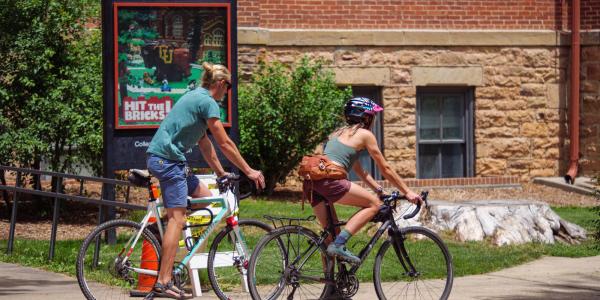 Cyclist ride past Old Main on June 21, 2022. (Photo by Glenn Asakawa/University of Colorado)