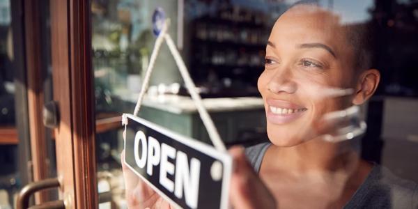 women looking at 'open' sign through window of business 