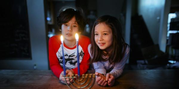 Two Asian American children look at a lit menorah