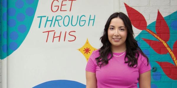 Mia Torres in front of a mural that says: We'll get through this