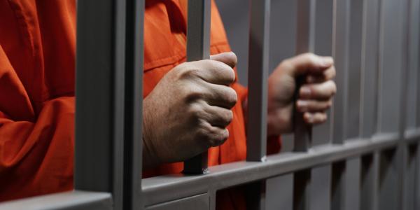 prisoner in orange jump suit grasping prison bars