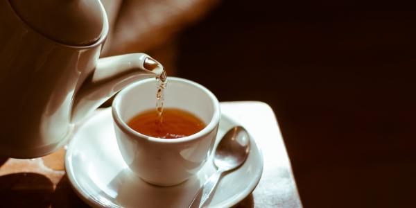 Tea is poured from a white kettle into a white cup. 