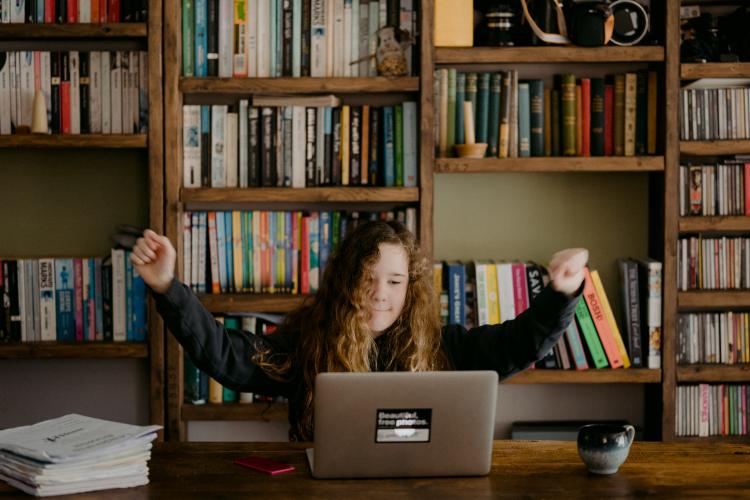 Student at computer with hands raised in celebration