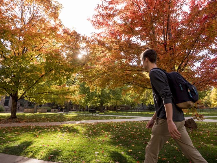 Student walks across campus with fall colors in background