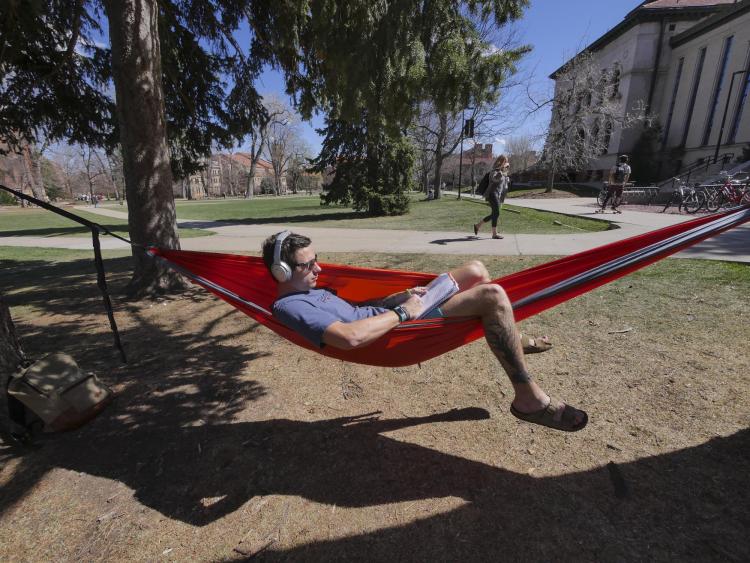 Student lounging in hammock reading on campus