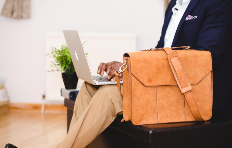 Man in suit types on laptop, with leather briefcase next to him