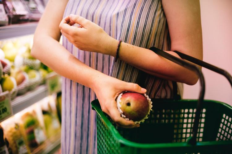 Woman puts red apple into her grocery shopping basket