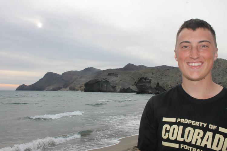 Austin Riley stands in his CU football shirt in front of the shoreline in Spain.