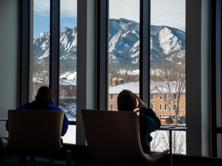 Students sitting in chairs looking through a window at snow-covered mountains