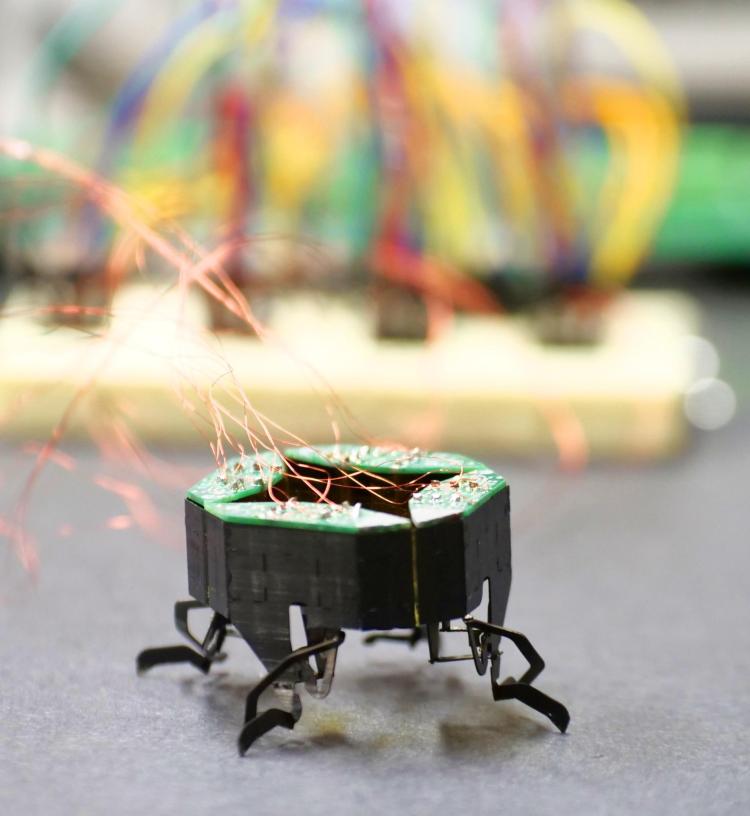 small robot with wires coming off of it stands on a table