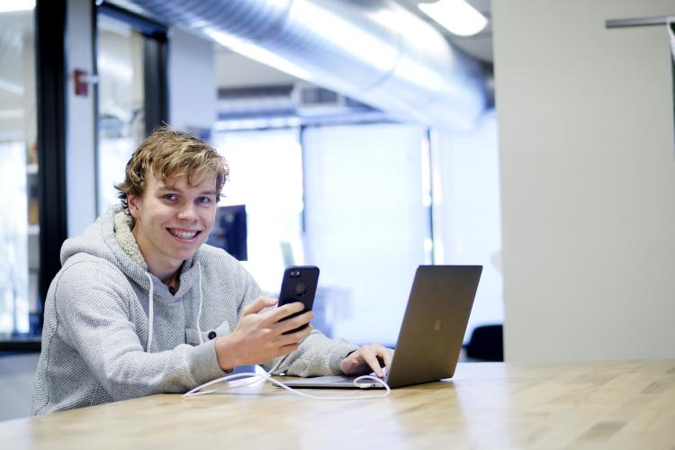 Cam Connor holds his phone while working on his laptop