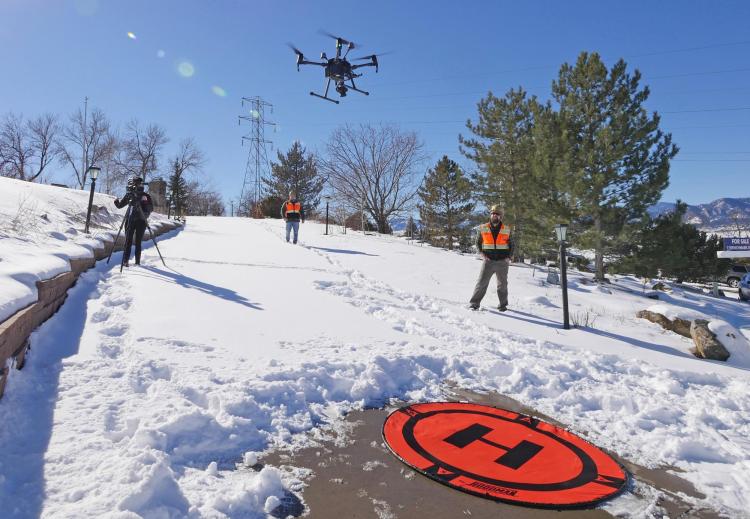 Members of the GEER team watch a drone take off from a snowy driveway