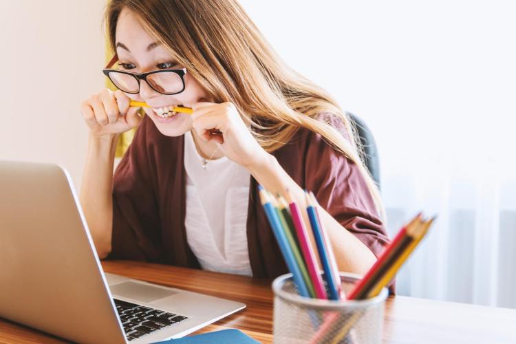 stressed out student bites pencil while looking at laptop computer