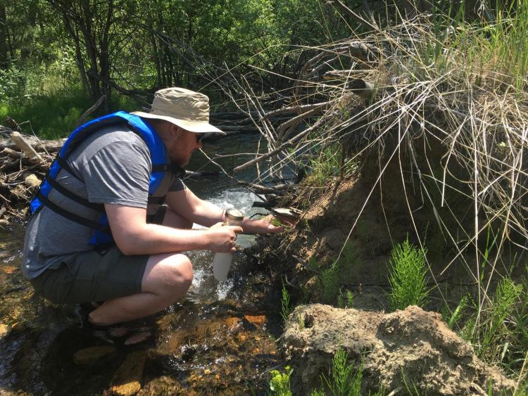 Researcher taking water sample in creek