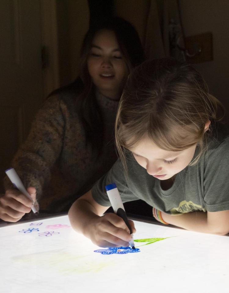 A child and a researcher play at a light table as part of a study