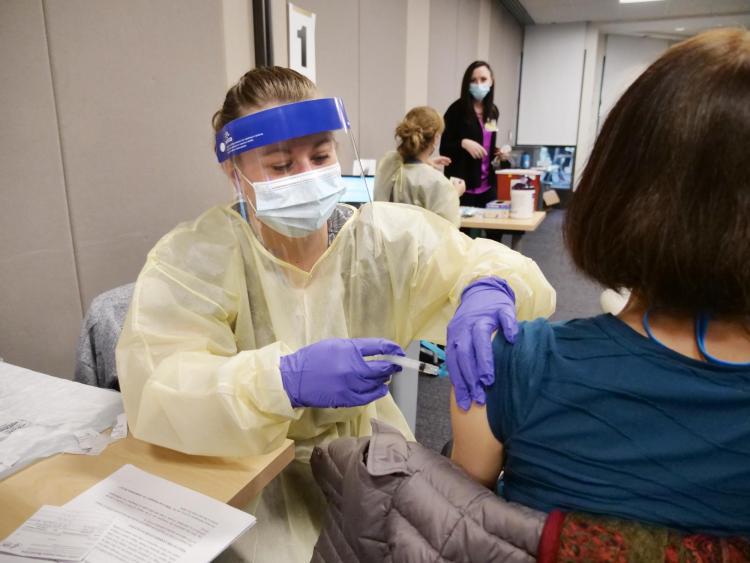 Nurse in wearing mask and face shield administers a vaccine