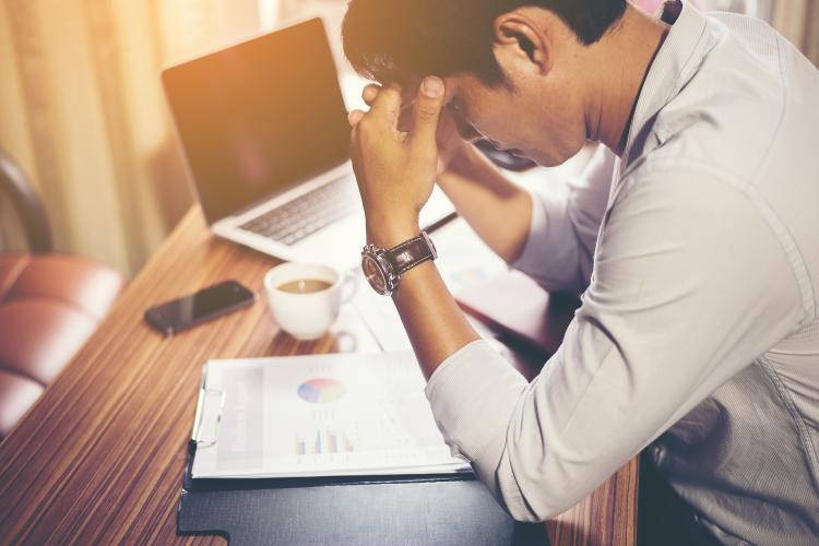 Stressed-out man sits at desk with face in hands