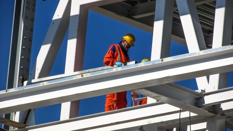 A construction worker in a helmet is seen surrounded by steel framing. 