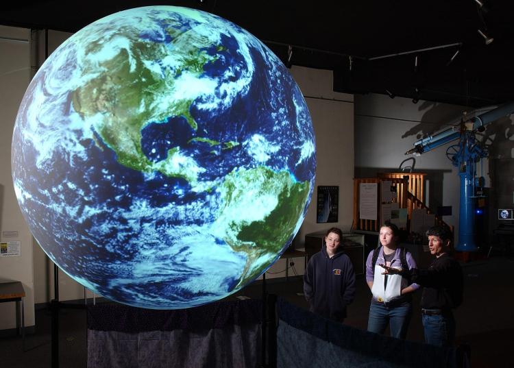 Community members look at huge, glowing model of Earth