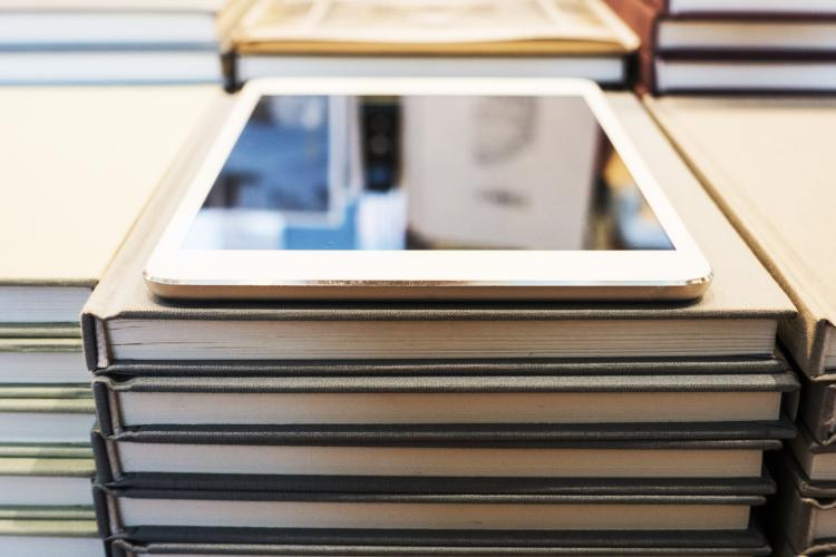 A modern digital tablet sits atop stacks of books.