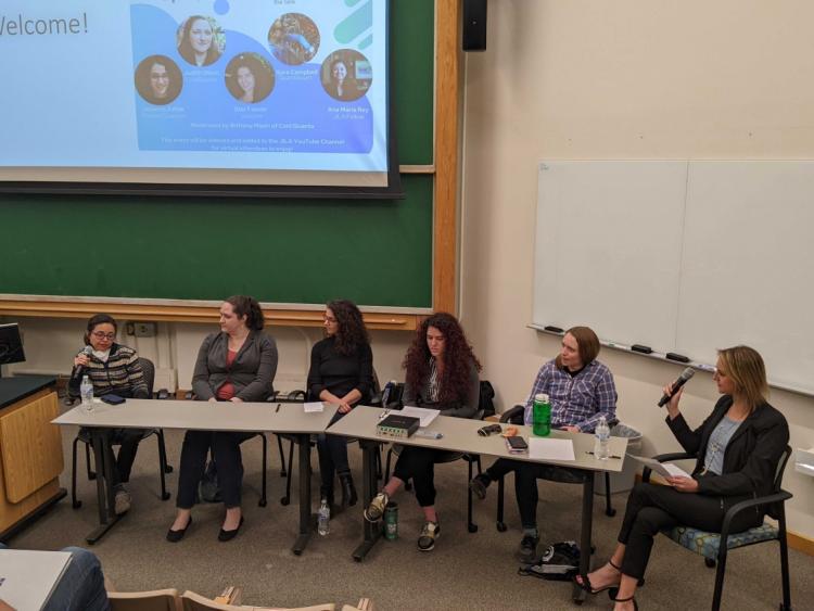 Panelists sit at a table in front of a projector screen