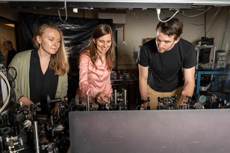 Three people stand at a scientific bench working on equipment