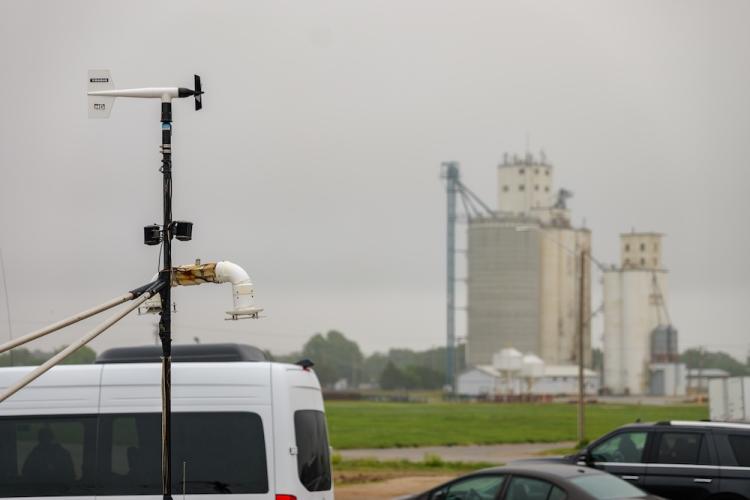 A weather vane sitting on a pole with grain silos in the background