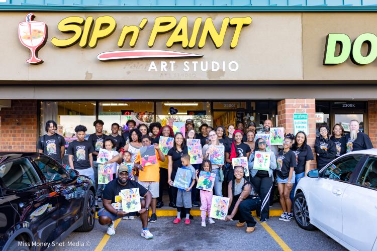 The Game Changers stand with community members at a sip and paint gathering.