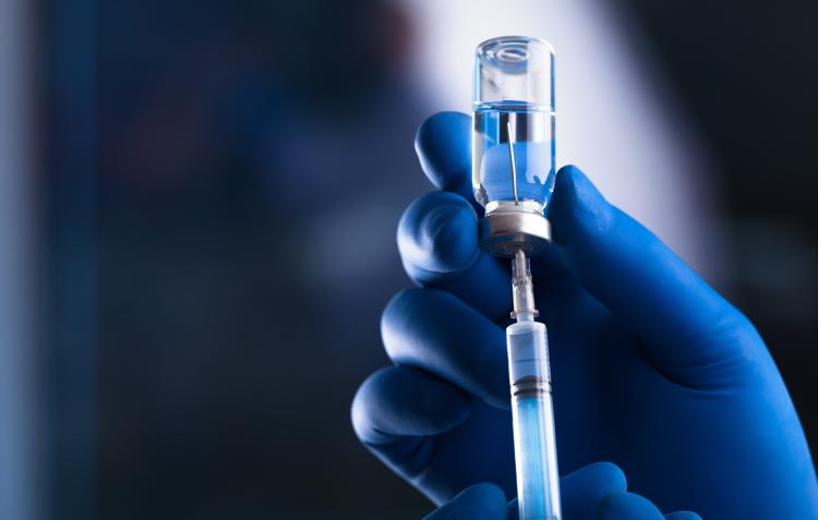 Gloved hands holding vaccine bottle and syringe