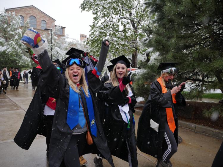 Graduates walk in commencement procession, some donning ski goggles in the snow